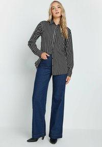 Camicia a righe bianco e nero con bottoni, maniche lunghe, abbinata a jeans a gamba larga blu scuro. Tessuto morbido con vestibilità su misura.