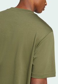 Olivovo zelené tričko s krátkymi rukávmi, okrúhlym výstrihom, vyrobené z mäkkého bavlneného materiálu, viditeľné švy na golieri a leme.