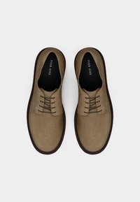 Καφέ παπούτσια από σουέντ με λεία επιφάνεια, διαθέτουν πέντε τρύπες για κορδόνια και αντίθετη σκούρα καφέ σόλα. Απλός σχεδιασμός, χωρίς σχέδια ή διακοσμήσεις.