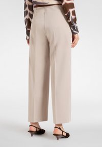 Beżowe spodnie typu wide-leg z gładkiego materiału, z wysokim stanem i prostym tyłem; zestawione z brązowymi butami na obcasie.