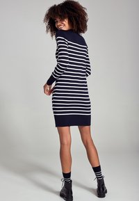 Robe-pull rayée bleu marine à manches longues, dotée de rayures horizontales blanches et d'une silhouette ajustée, associée à des bottes noires à la cheville.