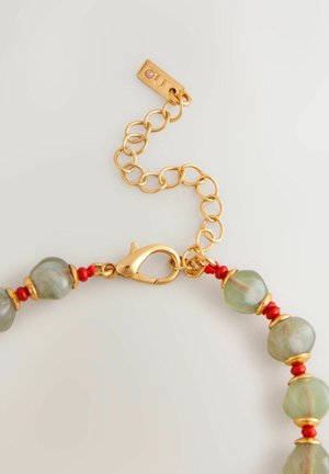 Gold chain bracelet featuring green beads interspersed with red accents, clamped lobster clasp, and small engraved tag.