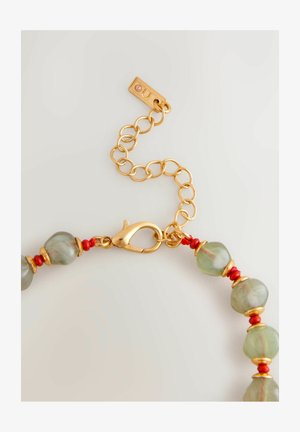 Gold chain bracelet featuring green beads interspersed with red accents, clamped lobster clasp, and small engraved tag.