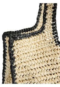 Gros plan d'un sac cabas en paille tressée beige avec garniture et anses tressées noires sur fond blanc.