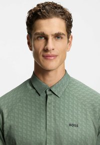 Camicia verde a fantasia con colletto button-down, tessuto testurizzato e marchio discreto sull'area sinistra del petto.