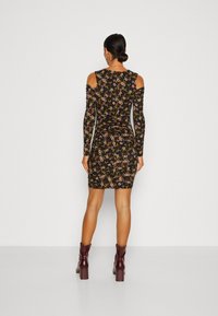 Černé květinové šaty s dlouhými rukávy a výřezy na ramenou, s přiléhavým střihem a řasenými detaily, doplněné vínovými kotníkovými botami na podpatku.