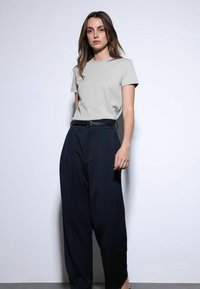 Lichtgrijs T-shirt met korte mouwen gecombineerd met een zwarte broek met hoge taille en een zwarte riem. Glad, lichtgewicht stof.