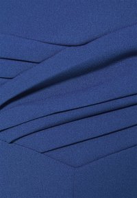 Mörkblått tyg med en texturerad yta, med diagonala veck och en slät finish. Designen inkluderar geometriska former nära sömmen.