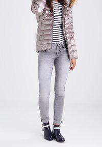 Lys grå pufferjakke med en hætte med pelsfor, stribet skjorte, tætsiddende grå jeans og marineblå ankelstøvler med hvide stropper og en blank finish.