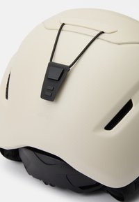 Cremfarbiger Helm mit schwarzen Akzenten, der ein stromlinienförmiges Design, verstellbare Riemen, Belüftungsöffnungen und einen Regler zur Anpassung der Passform aufweist.