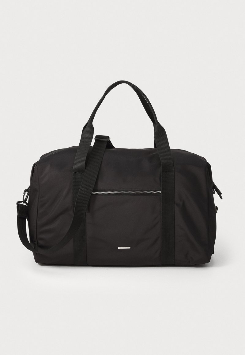 Zwarte duffelbag van duurzaam nylon. Beschikt over dubbele handgrepen aan de bovenkant, een verstelbare schouderband en een voorzak met rits. Soepele textuur.