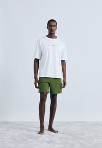 Λευκό υπερμεγέθες μπλουζάκι με το λογότυπο "TOMMY HILFIGER", συνδυασμένο με πράσινα σορτς. Απλός σχεδιασμός, κοντά μανίκια και άνετη εφαρμογή.