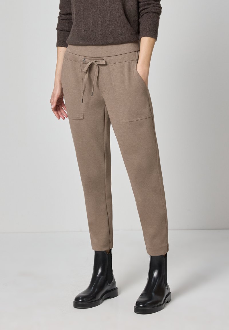 Beige joggingbroek met een ontspannen pasvorm, trekkoord in de taille en twee zijzakken, gecombineerd met zwarte enkellaarsjes. Gladde stoftextuur.
