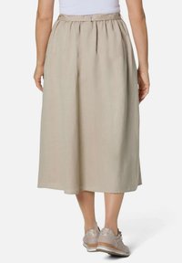 Beige Leinen-Midikleid mit einem gerafften Taillenbund und seitlichen Taschen, kombiniert mit hellgrauen Sneakers mit strukturierten Akzenten.