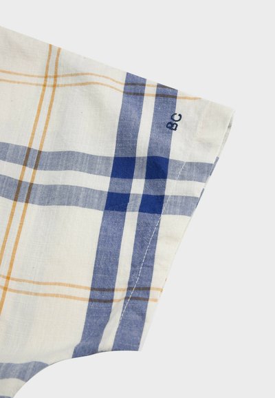 Coin d'un tissu blanc à carreaux bleus et beiges avec de petites initiales "BC" brodées sur le bord.