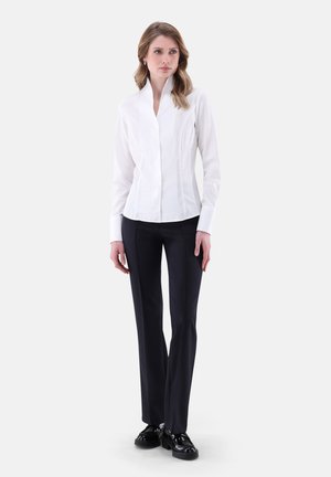 Weißes Hemd mit hohem Kragen und figurbetontem Design, kombiniert mit schwarzen geraden Hosen und schwarzen Schuhen. Einfacher, strukturierten Look.