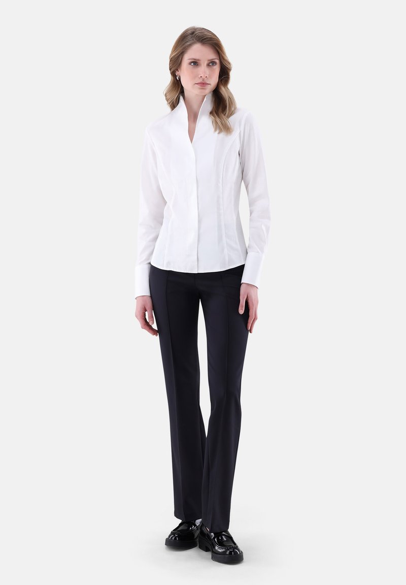 Weißes Hemd mit hohem Kragen und figurbetontem Design, kombiniert mit schwarzen geraden Hosen und schwarzen Schuhen. Einfacher, strukturierten Look.