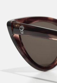 Cat-eye sunglasses with a dark tortoiseshell frame, gray lenses, and a sleek black temple featuring a logo detail. Smooth, glossy finish.