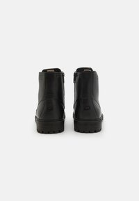 Botas de tobillo de cuero negro con una textura suave, cremalleras laterales y una suela de goma resistente con surcos profundos. Con un diseño marcado por un branding minimalista.