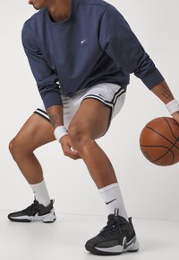 Sweatshirt azul marinho com logótipo branco da Nike. Calções de basquetebol brancos com detalhes pretos. Ténis preto e branco. Pessoa a driblar uma bola de basquetebol.