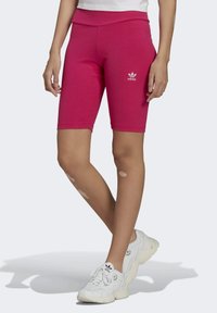 Różowe prążkowane spodenki rowerowe z wysokim stanem i wyszywanym białym logo adidas. Noszone z białymi trampkami, prezentujące swobodny sportowy look.