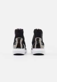 Para czarnych sneakersów za kostkę z metalicznymi srebrnymi elementami na piętach i białymi podeszwami, przedstawionych z tyłu na białym tle.