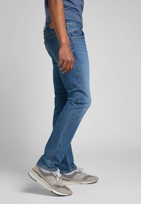 Ciemnoniebieskie dżinsy o dopasowanym kroju z jasnym przecieraniem, połączone z szarymi trampkami z białymi akcentami i sznurówkami.