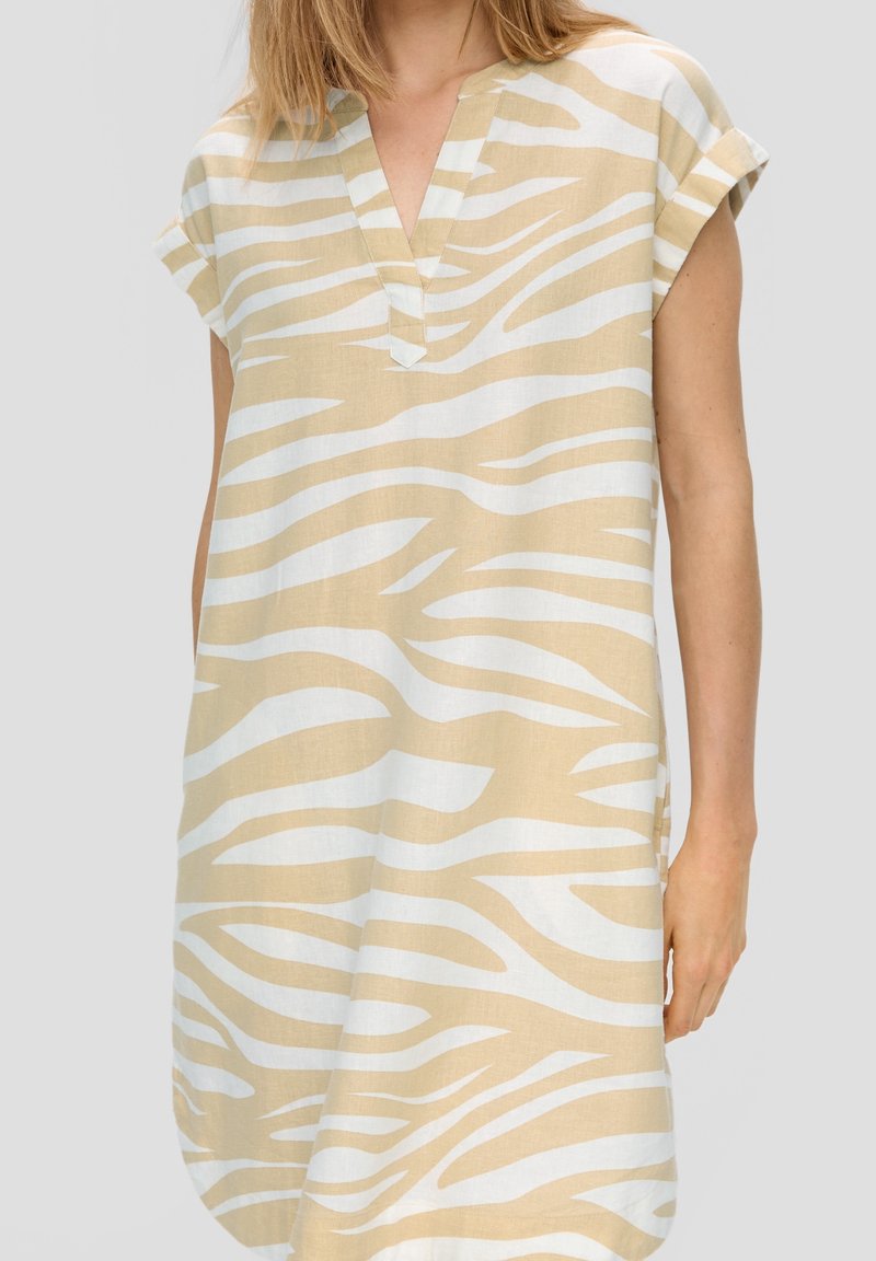 Robe courte beige avec un col en V et des manches courtes. Présente un motif à rayures zébrées blanches. Confectionnée dans un tissu léger.