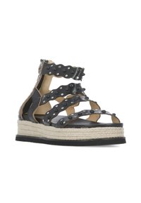 Sandalo in pelle nera con cinturini ondulati, borchie argentate e suola in juta stile espadrilles. Presenta tacco aperto e suola piatta in gomma.