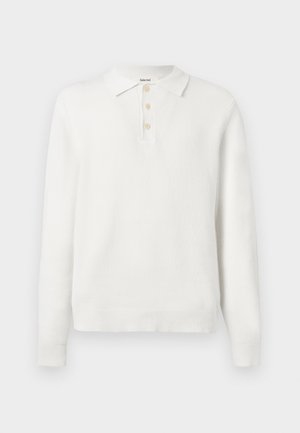 Polo shirt en tricot blanc à manches longues avec col et trois boutons beiges sur le plastron, présenté sur un fond clair uni.