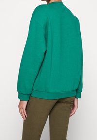 Grön bomullströja med avslappnad passform, rund halsringning och ribbstickade ärmar. Matcher med olivgrön byxa som har en slät textur.