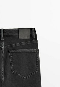 Gros plan sur l'arrière d'un jean en denim noir présentant une poche unique et une étiquette en cuir de marque au-dessus de la taille.