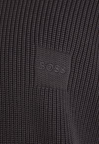 Dark gray knitted fabric with ribbed texture featuring a small embossed "BOSS" logo patch in matching color.
