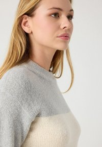 Suéter en gris claro y crema con cuello redondo, textura de punto y diseño a bloques de color. Tejido suave y corte entallado.