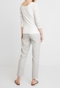 Vit spets långärmad topp med rundad halsringning, tillsammans med ljusgrå linnbyxor. Outfiten har en avslappnad passform och subtila texturer.