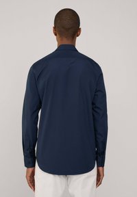 Camisa de manga larga azul marino hecha de tela suave, con un collar clásico y puños abotonados. Dobladillo curvado y sutil detalle en la yugo trasero.