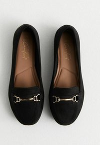 Mocassins en suede noir avec un bout rond, accent en métal doré à l'avant et une doublure intérieure lisse. Semelle plate, design simple.