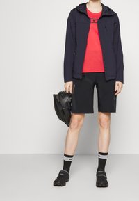 Outdoor apparel featuring a navy jacket, red shirt, black shorts, and black shoes. Accessories include a gray and black helmet.