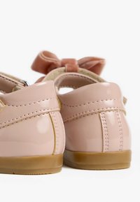 Chaussures en cuir verni rose avec une finition brillante, bout rond et un nœud à l'arrière, dotées d'une semelle en caoutchouc beige.