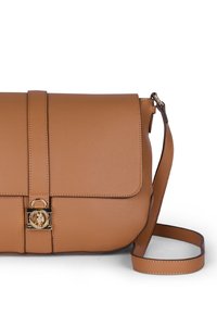 Tan læder crossover-taske med klap, guldfarvede hardware og logo detalje. Har en justerbar strop og pebble-textureret overflade.