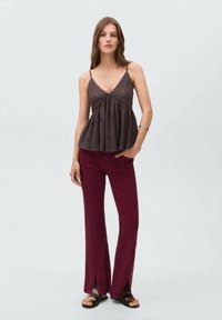 Haut sans manches marron foncé avec un décolleté en V et une taille froncée, associé à un pantalon évasé bordeaux avec des fentes latérales et des sandales noires.
