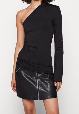 Femme portant un top noir asymétrique à manches longues avec côtés froncés, associé à une mini-jupe en cuir noire avec fermeture éclair devant.