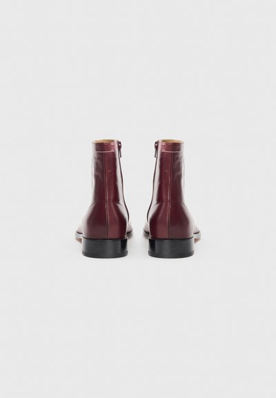 Burgundy läderankelboots med en slät finish, sidodragskedja och svarta gummisulor. Minimalistisk design med en smidig silhuett.