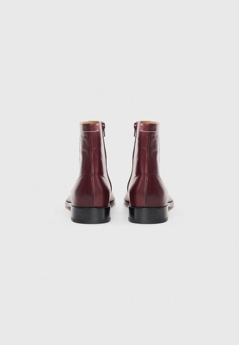 Burgundy läderankelboots med en slät finish, sidodragskedja och svarta gummisulor. Minimalistisk design med en smidig silhuett.