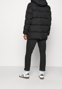 Sort dunjakke med hætte, quiltet design og høj krave, parret med mørke, tapered bukser og hvide sneakers med sorte detaljer.
