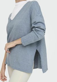 Camicia azzurro chiaro a maniche lunghe con scollatura a V, fessure laterali e polsini a costine. Realizzata in un tessuto morbido, presenta una vestibilità oversized e una silhouette rilassata.