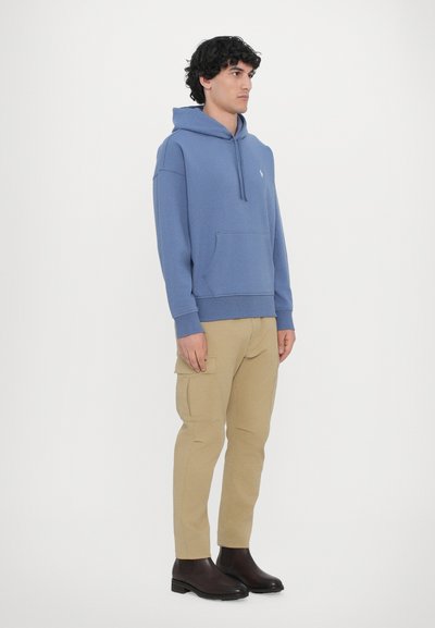 Blå bomulds-hoodie med frontlomme, parret med beige cargo-bukser og brune ankelstøvler. Simpelt design, afslappet pasform og struktureret stof.