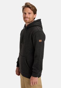 Felpa grigia scura con tasca a marsupio, cappuccio regolabile con coulisse, polsini a coste e un piccolo patch in pelle marrone sulla manica.