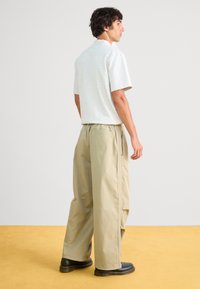 Ανοιχτό γκρι κοντομάνικο πουκάμισο συνδυασμένο με χαλαρούς μπεζ παντελόνες. Οι παντελόνες διαθέτουν ελαστική μέση, πλαϊνές τσέπες και λεία υφή.