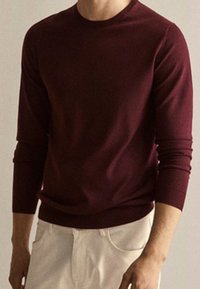 Maglione bordeaux a maniche lunghe realizzato in tessuto morbido, con scollo rotondo e polsini aderenti, abbinato a pantaloni chiari.